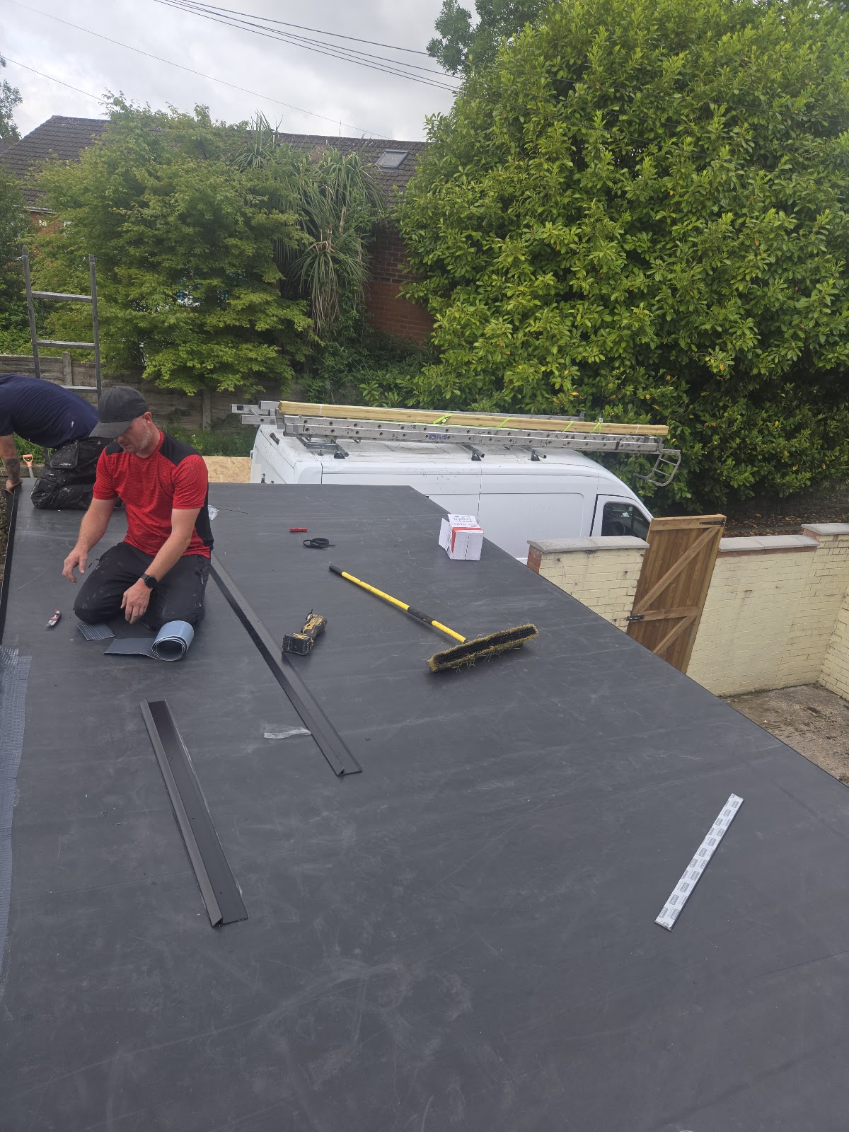 Two workers on a flat roof with tools and strips of roofing material